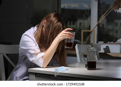 Female Doctor Sitting At The Table And Hold Glass With Whiskey Or Cognac At Home After Hard Work, Depressed Female Drinking Strong Alcohol Suffering From Coronavirus Problems