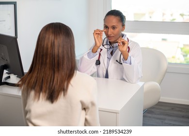 Female Doctor Sitting At Table And Talking To Patient. Young African American General Practitioner Consulting Woman In Her Office. Visit To Doctor Concept