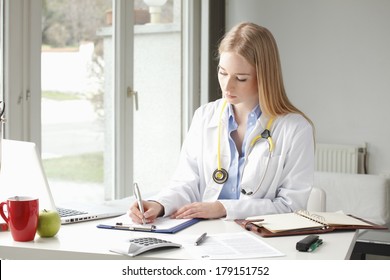 Female doctor sitting and writing at desk in clinic. Stock Photo