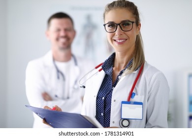 Female Doctor Smiling And Holding Clipboard From Behind Her Colleague Is Standing. Medina Services Of All Directions Concept