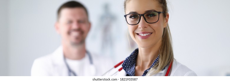 Female Doctor Smiling And Holding Clipboard From Behind Her Colleague Is Standing. Medina Services Of All Directions Concept