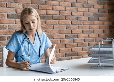 Female Doctor With Stethoscope Filing Papers, Checking Patient History Form, Reviewing Reports Or Medical Records. Nurse In Blue Uniform Working In Office At Hospital. Concept Of Social Insurance