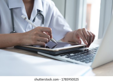 Female Doctor Taking Notes On Digital Tablet And Working On Laptop Computer Recording Information In Doctor Office In Hospital. Medical Student Recording Case Study On Tablet Pc In Medical School