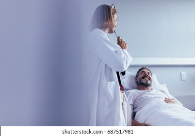 Female doctor talking to male patient lying in hospital bed. Medical professional interacting with patient in hospital ward. - Powered by Shutterstock