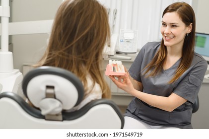 Female doctor talking to a young woman patient. Discussion of the treatment plan. The dentist shows a model of a dental implant. Modern dental clinic - Shutterstock ID 1971549719