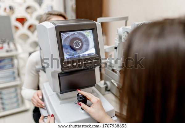 Female doctor testing person for her eyes with\
special optical\
apparatus.