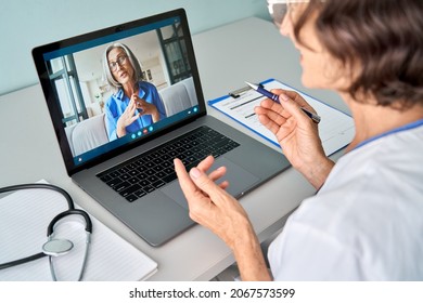 Female Doctor Therapist Consulting Older Senior Patient Via Virtual Video Call Visit Using Laptop Computer. Digital Online Healthcare, Distance Telemedicine. Telehealth Videocall. Over Shoulder View