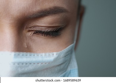 A female doctor therapist in a white robe, mask and gloves. Face close-up. The doctor cries and prays. Tears in eyes. Regret, anxiety and despair. Pandemic and virus epidemic. Coronavirus covid-19.