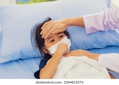 Female doctor touching forehead attentive treating influenza symptoms young girl who is sick weak infected with virus wearing medical mask treating the sick hospital bed hospital treatment room.  - Powered by Shutterstock