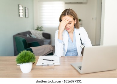 Female Doctor Touching Her Forehead And Looking Stressed And Overwhelmed While Doing Some Paperwork At Home