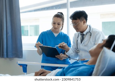 A female doctor and two male doctors treat a young male patient in bed and are talking to an Asian male patient beside the hospital bed in a hospital emergency room. - Powered by Shutterstock