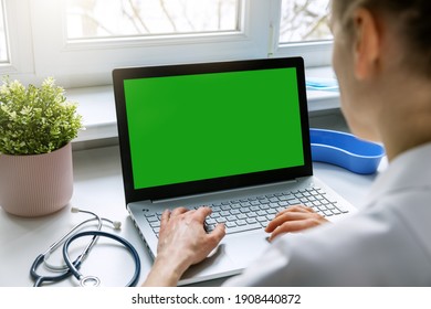 Female Doctor Typing On Her Laptop Computer In Medical Clinic Office. Blank Green Screen Mockup