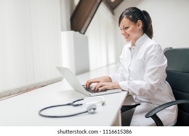 Female Doctor Typing Report With Laptop.