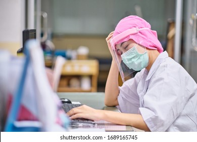 Female Doctor Under Stress And Headache Sleeping In Front Of Computer, Wearing Hospital Scrub, Face Shield, Mask Protection, Concept Of Health Care Provider Front Line Against Corona Virus COVID-19