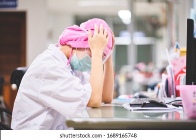 Female Doctor Under Stress And Headache Working Hard In Front Of Computer, Wearing Hospital Scrub, Face Shield Mask Protection, Concept Of Health Care Provider Front Line Against Corona Virus COVID-19