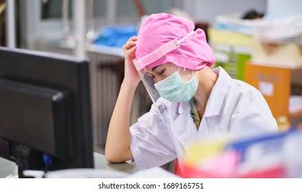 Female Doctor Under Stress And Headache Sleeping In Front Of Computer, Wearing Hospital Scrub, Face Shield, Mask Protection, Concept Of Health Care Provider Front Line Against Corona Virus COVID-19