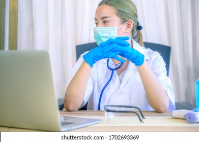 Female Doctor Under Stress And Headache Sleeping In Front Of Computer, Wearing Hospital Scrub, Face Shield, Mask Protection, Concept Of Health Care Provider Front Line Against Corona Virus COVID-19