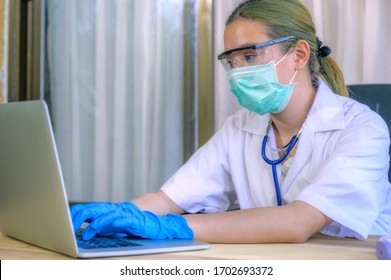 Female Doctor Under Stress And Headache Sleeping In Front Of Computer, Wearing Hospital Scrub, Face Shield, Mask Protection, Concept Of Health Care Provider Front Line Against Corona Virus COVID-19