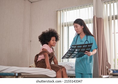 Female Doctor In Uniform Health Checks A Child, Illness Patient, Diagnosis Explains X-ray Film In Emergency Room Bed At Hospital Ward, Pediatric Clinic, Kids Examination Consult.