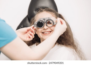 A female doctor uses special glasses to diagnose a patient’s eyes and select lenses in the clinic. Ophthalmology concept. An optician checks the vision of a small child. - Powered by Shutterstock