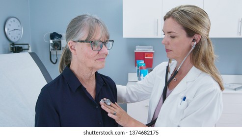 Female Doctor Using Stethoscope Listening To Senior Patients Heart. Older Woman Visiting Her Primary Care Physician For A Regular Check Up