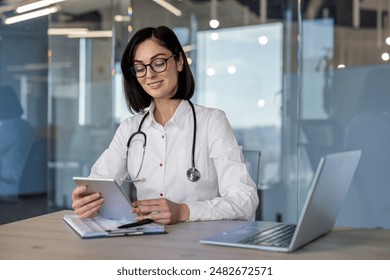 Female doctor using tablet computer at office . Modern medical professional wearing stethoscope, working with technology at workplace. Confident, focused healthcare provider reviewing information. - Powered by Shutterstock