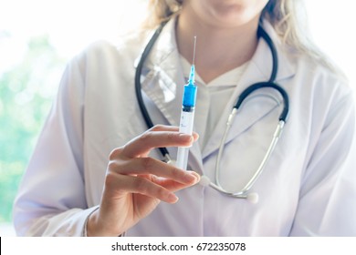 Female Doctor With Vaccination Syringe In Hand Wearing White Jacket And Stethoscope Ready For Injection For Infectious Disease. Healthcare And Infection Control Concept