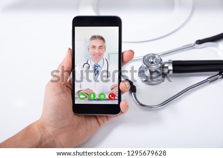 Female Doctor Video Conferencing With Happy Male Colleague On Cellphone Over Desk