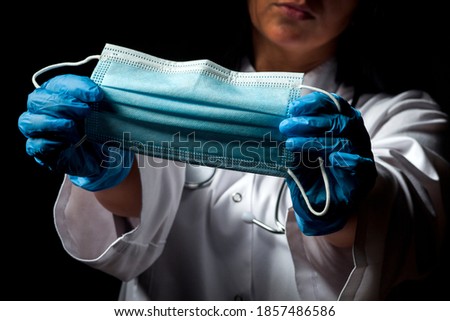 Female doctor wearing a disposable protective mask against covid-19 coronavirus infections on a black background