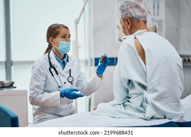 Female Doctor Wearing Face Mask While Explaining To Senior Patient What Medicines He Should Take After Medical Checkup At The Clinic.