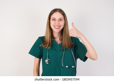 Female doctor wearing a green scrubs and stethoscope is on white background doing happy thumbs up gesture with hand. Approving expression looking at the camera showing success. - Powered by Shutterstock