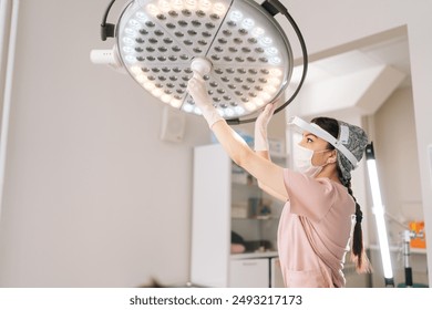 Female doctor wearing medical uniform adjusting light preparation performing operation at hospital. Surgeon adjusting surgical lamp before medical procedure. Concept of professional health treatment. - Powered by Shutterstock