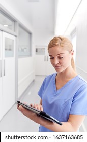 Female Doctor Wearing Scrubs In Hospital Corridor Using Digital Tablet