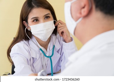 The Female Doctor Wearing A Surgical Mask And Using A Stethoscope To Check The Pulse And Look At A Male Patient, Focus On The Doctor.