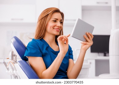 Female doctor wearing uniform sitting in ER using tablet computer checking patient's medical records and smiling with copy space - Powered by Shutterstock