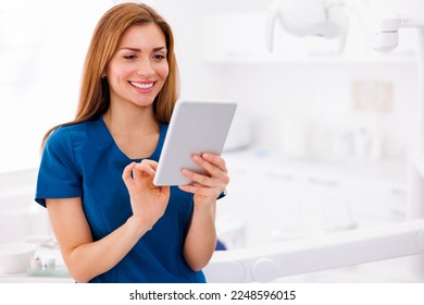 Female doctor wearing uniform standing in ER using tablet computer checking patient's medical records and smiling with copy space - Powered by Shutterstock