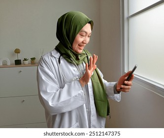 Female Doctor In White Cloak Waving Hand To Patient Or Family While Having Video Call On Smartphone In Office - Powered by Shutterstock