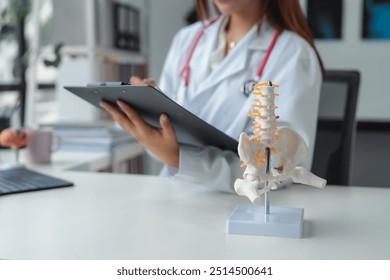 Female doctor in a white coat analyzes a spine model in a medical office during the day, showing expertise in healthcare - Powered by Shutterstock