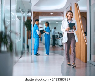 Female Doctor In White Coat With Digital Tablet In Hospital With Colleagues In Background - Powered by Shutterstock