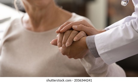 Female doctor in white coat holding hand of senior patient, giving help, comfort, psychological support, empathy at appointment. Elderly medic care, geriatric healthcare concept. Close up
