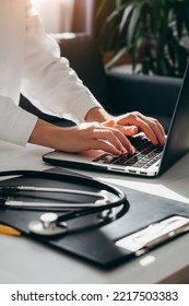 Female Doctor In White Coat With Stethoscope Using Laptop, Writing In Medical Journal, Professional Therapist Practitioner Sitting At Table In Hospital And Typing At Computer. Medicine Concept