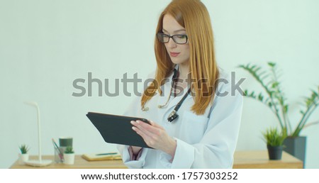 Female doctor in white coat using modern TabletPC device with touch screen. Doctor using DigitalTablet texting to patient informing about medical test results.