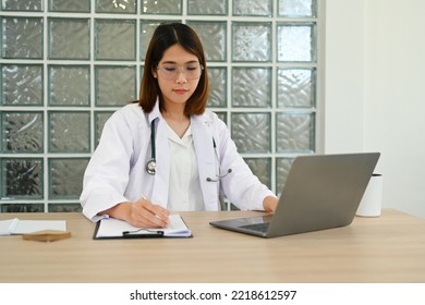 Female Doctor In White Coat Writing Filling Medical Form And Watching Online Medical Webinar Seminar Training On Laptop Computer