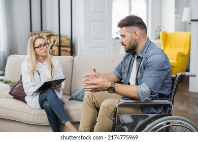 Female Doctor In White Lab Coat Holding Clipboard In Hands While Consulting Disabled Man During Visit At Home. Concept Of Rehabilitation, People And Medical Treatment.