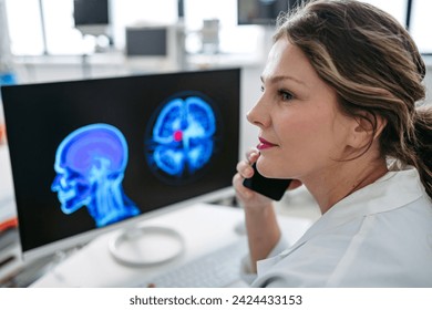 Female doctor working on computer in doctor's office, looking at MRI scan, phone calling test results to patient. Doctor consulting scan with other doctors. - Powered by Shutterstock