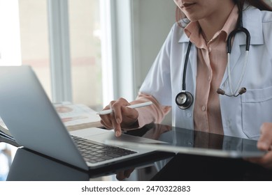 Female doctor working on laptop computer searching the information and using digital tablet at doctor's office. Medical student using computer, healthcare and medicine concept - Powered by Shutterstock