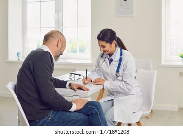 Female Doctor Writing Medication Order For Senior Patient In Clinic. Elderly Man On Visit To His Healthcare Provider