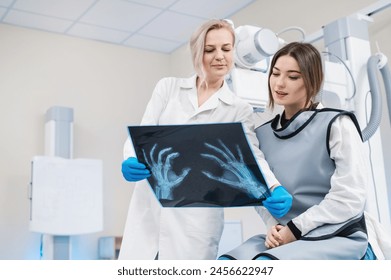 a female doctor and a young female patient look at an x-ray of hands, fingers and rejoice in the radiology room against the background of medical equipment. No bone fracture.	 - Powered by Shutterstock