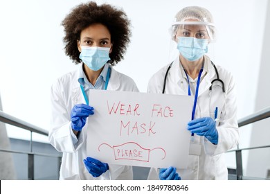 Female Doctors Holding Placard With 'wear Face Mask' Text As Appeal During Coronavirus Pandemic.