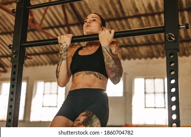 Female doing pull up workout in empty factory shade. Tattooed woman in sportswear exercising at an abandoned warehouse. - Powered by Shutterstock